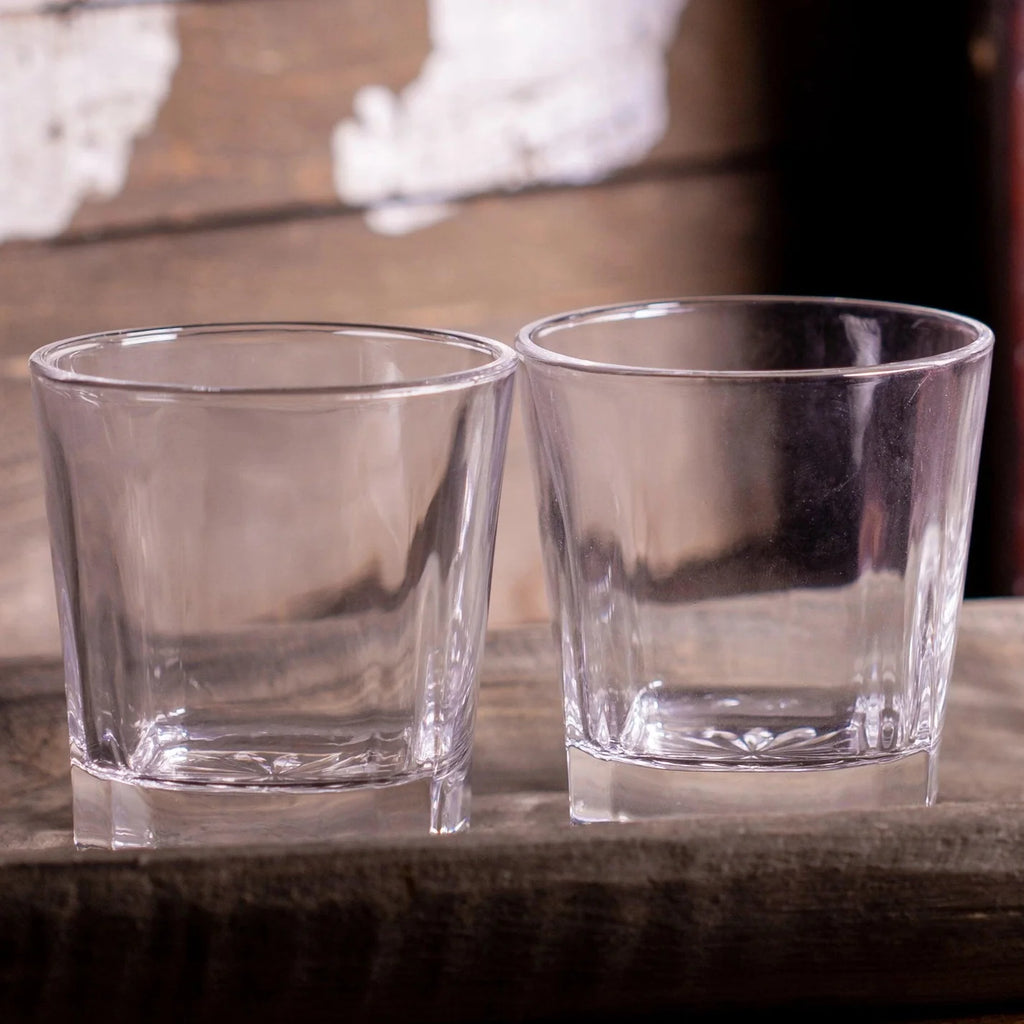 Two clear whiskey rocks glasses sitting on a rustic wood surface
