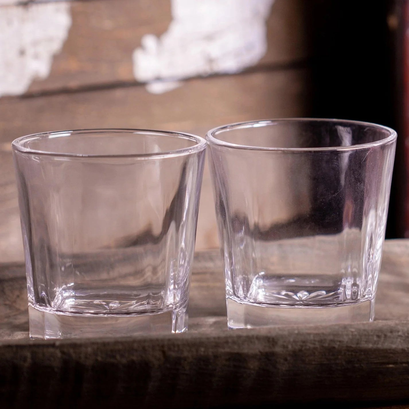 Two clear whiskey rocks glasses sitting on a rustic wood surface